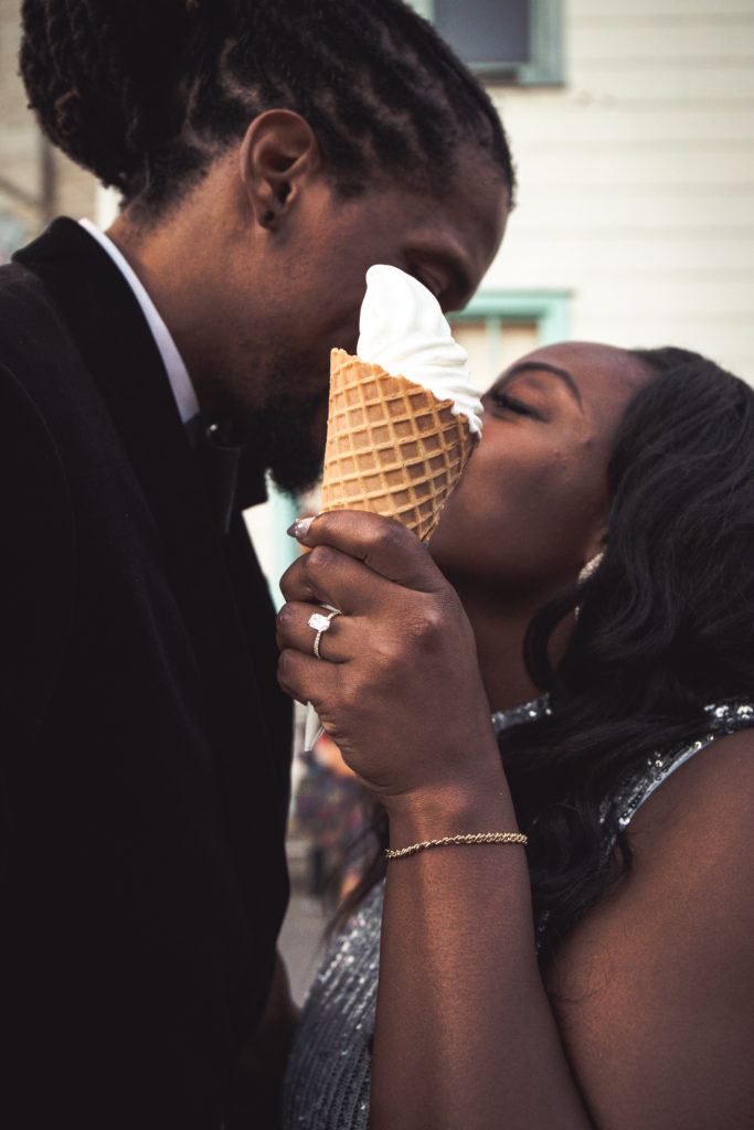 Black Couple kissing behind a soft serve ice cream cone in front of Ample Hills Creamery at Brooklyn Bridge Park, Pier 1
