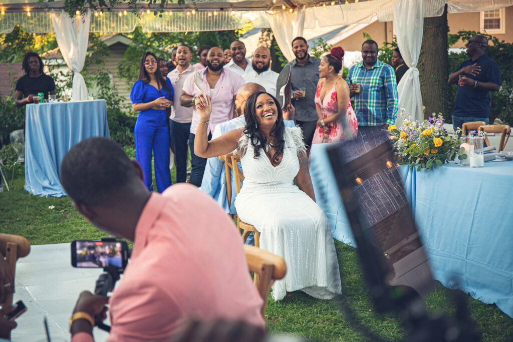 A beaming couple at their small wedding engaged in a unique shoe game. As interactive entertainment, they surrounded by their intimate group of guests, creating a memorable and enthralling experience.