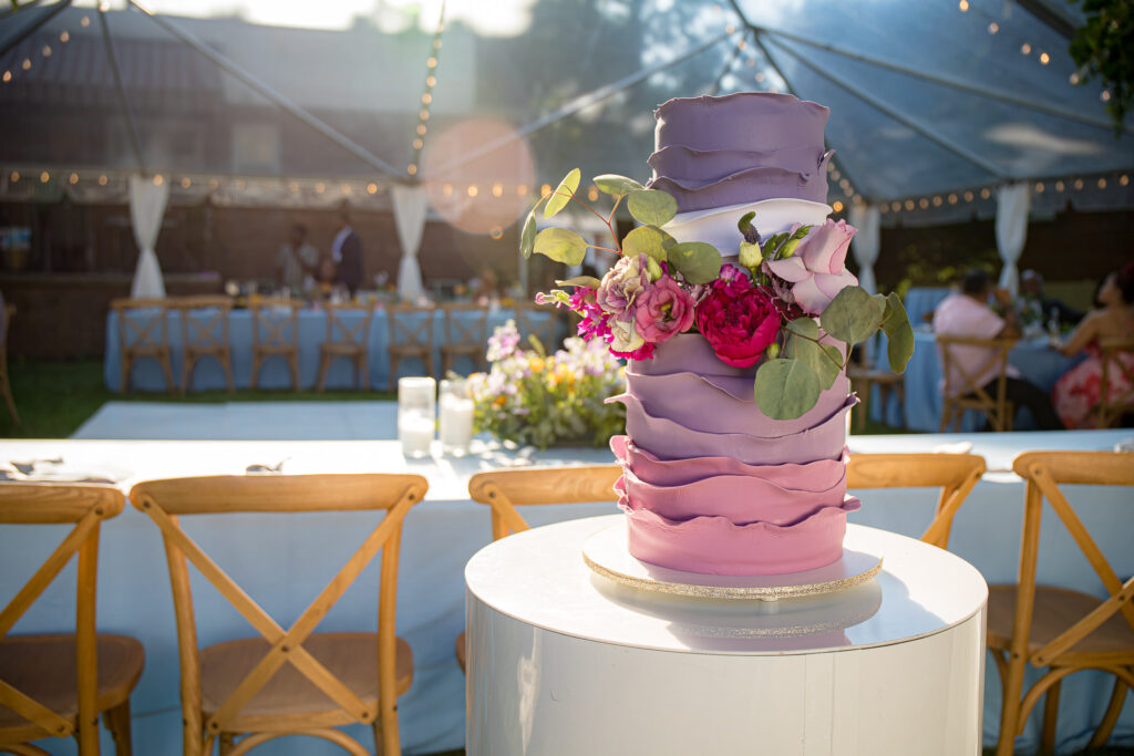 Lavender tiered wedding cake adorned with flowers at an outdoor micro-wedding reception.